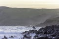 Surfer standing on rocky shore attempting evening surf in rough sea