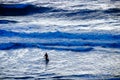 Surfer striding towards big waves in turbulent sea at dusk Royalty Free Stock Photo