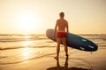 Surfer with surfboard looking at sunset at Goa India