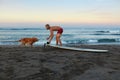 Surfer. Surfing Man Playing With Dog Near Surfboard On Sandy Beach. Royalty Free Stock Photo