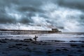 Surfer waiting on the shoreline holding his board on a cloudy day