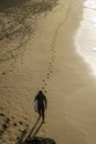 A surfer walks on a sandy beach at sunset, leaving behind the footprints on the golden sand Royalty Free Stock Photo