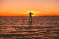 Surfer woman stand up paddle boarding at dusk on a flat warm quiet sea with beautiful sunset colors Royalty Free Stock Photo