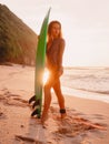 Surfer woman in swimwear hold surfboard at tropical beach with sunset tones Royalty Free Stock Photo