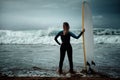 Surfer woman wearing wetsuit standing on the beach with a surfboard