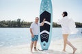 Surfers couple on the beach. Man stand with paddleboard and smiling. He waiting his partner. Young beautiful woman in sunglasses Royalty Free Stock Photo