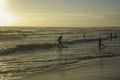 Surfers having surf lessons riding down small waves in sunset on beach in spain