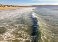 Surfers in the water with a wave breaking and beautiful Southern California beach stretching to the horizon Royalty Free Stock Photo