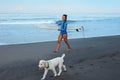 Surfing Girl. Beautiful Woman Walking With Dog On Sandy Beach. Smiling Brunette In Blue Wetsuit Carrying Surfboard. Royalty Free Stock Photo