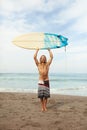 Surfing. Handsome Surfer Holding White Surfboard Above Head. Smiling Man Standing On Sandy Beach Portrait.