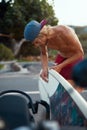 Surfing. Handsome Surfer Waxing White Surfboard On Beach Road. Young Tanned Guy In Cap.