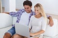 Surfing the net together. A happy couple sitting together on a couch in their living room and using a laptop together. Royalty Free Stock Photo