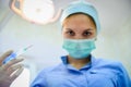 The surgeon dentist in mask holding syringe leaning over patient for injecting anesthesia