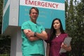 Surgeon or Doctor or Physician or Clinician and Asian Nurse Stand in Front of Hospital Emergency Room Sign