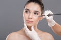 Surgeon drawing marks on female face against gray background