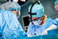 Surgeon and his assistant performing cosmetic surgery in hospital operating room. Surgeon in mask wearing loupes during Royalty Free Stock Photo
