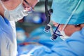 Surgeon and his assistant performing cosmetic surgery in hospital operating room. Surgeon in mask wearing loupes during Royalty Free Stock Photo