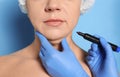 Surgeon with marker preparing woman for operation against blue background. Double chin removal