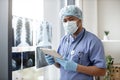 Surgeon posing with tablet near X-ray images in workplace