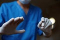 Surgeon`s hands in sterile latex gloves hold a surgical metal scalpel against the background of a bright lamp.
