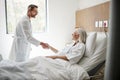 Surgeon Visiting And Shaking Hands With Mature Female Patient In Hospital Bed