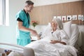 Surgeon Visiting And Shaking Hands With Mature Female Patient In Hospital Bed