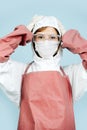 Surgeon in white gown adjusting her hood. wearing red leather apron and sleeves