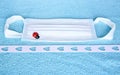 Surgical or medical mask, typical 3-ply doctor mask with lucky charm ladybird, blue towel as a background and hearts decoration