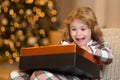 Surprise child opening Christmas magic presents. Happy funny child in winter pajama open Christmas gift near Christmas Royalty Free Stock Photo