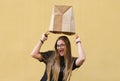 Surprise girl wearing a paper bag over her head in front of yellow background Royalty Free Stock Photo