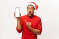 Surprised african american man in santa hat pointing at mobile phone with blank screen Royalty Free Stock Photo