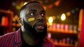 Surprised african-american man with spanish flag on cheek watching bed news Royalty Free Stock Photo