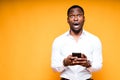 Surprised african american man in white shirt looking at camera holding phone in hands Royalty Free Stock Photo