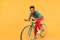 Surprised african guy in red pants riding on bike. Indoor photo of funny black young man sitting on Royalty Free Stock Photo