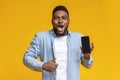 Surprised african man holding smartphone and showing thumb up