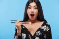 Surprised Asian woman eating sushi and rolls on a blue background. Black Friday sushi sale. Royalty Free Stock Photo