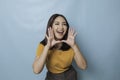 Surprised Asian woman reclines on her hands and shouting while looking at the camera over blue background