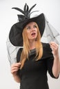 Surprised attractive blond woman in black witch hat with green eyes looks up. Young witch, vertical frame. Halloween party, white