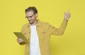 Surprised attractive man in glasses looking into tablet and pointing above over yellow background Royalty Free Stock Photo