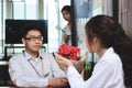 Surprised attractive young Asian woman accepting a bouquet of red roses from boyfriend with envious angry woman background on vale