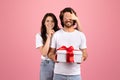 Surprised bearded man in a white shirt unknowingly holds a gift with a red ribbon as a smiling woman Royalty Free Stock Photo