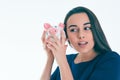 Beautiful Caucasian brunette woman listens to the sound of coinsin a piggybank and dreams. Royalty Free Stock Photo