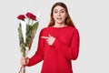 Surprised beautiful woman with cheerful expression, dark eyebrows, points at beautiful bouquet of roses, wonders recieving present