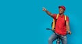 Surprised black delivery man riding bicycle pointing at copyspace Royalty Free Stock Photo