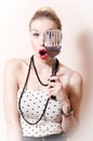 Surprised blond pinup pretty woman in polka dot dress looking through spatula on white background portrait Royalty Free Stock Photo