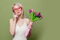 Surprised blonde girl with tulips on green background