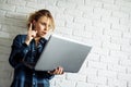 Surprised blonde woman with laptop iand standing against white brick wall.