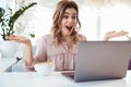 Surprised blondy woman in blouse sitting by the table