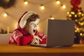 Surprised boy in Christmas festive clothing and hat watching movie online on laptop Royalty Free Stock Photo