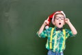 surprised boy in red christmas hat near a green chalkboard showing finger up Royalty Free Stock Photo